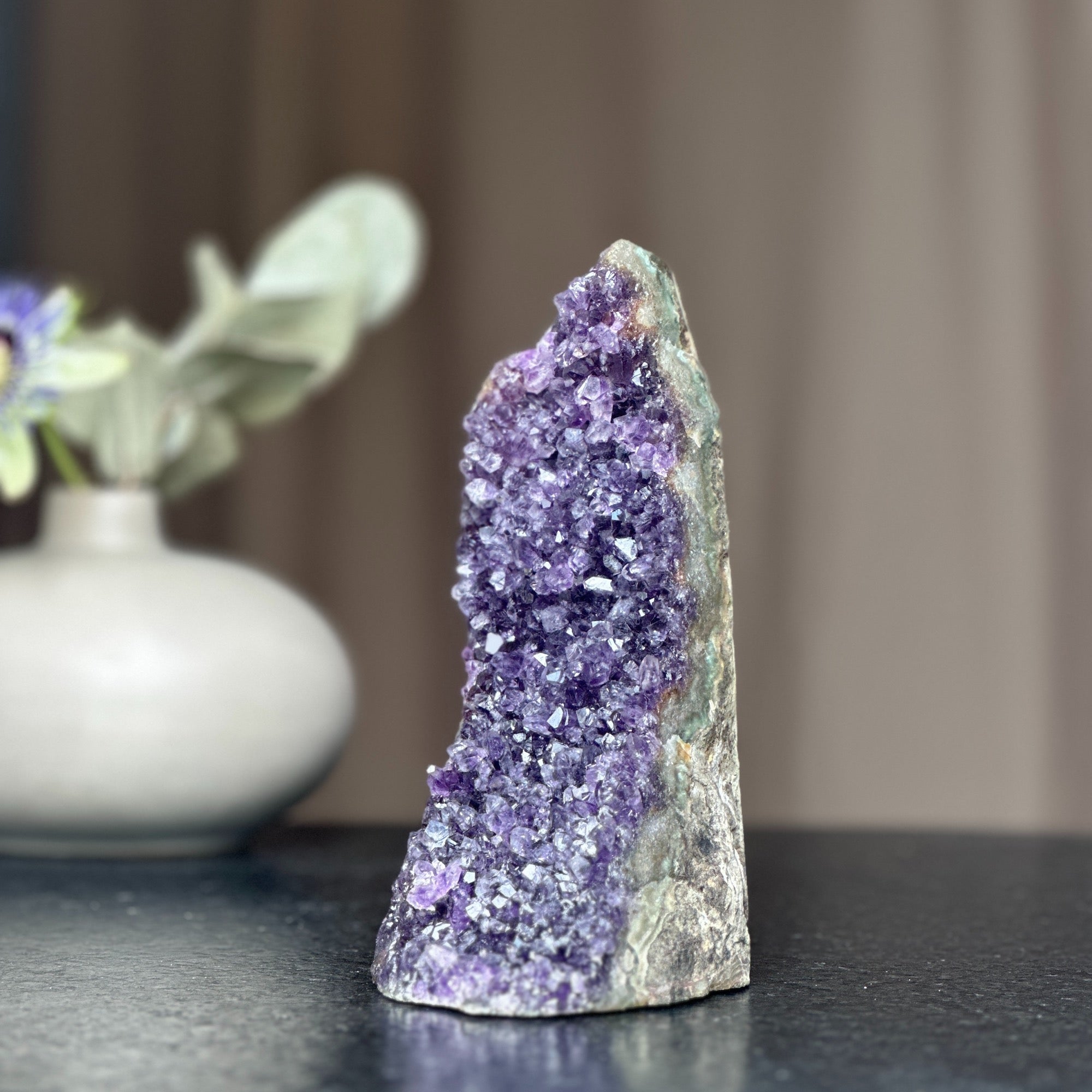 Tall, deep purple amethyst crystal cluster with a cut base, standing on a dark surface.