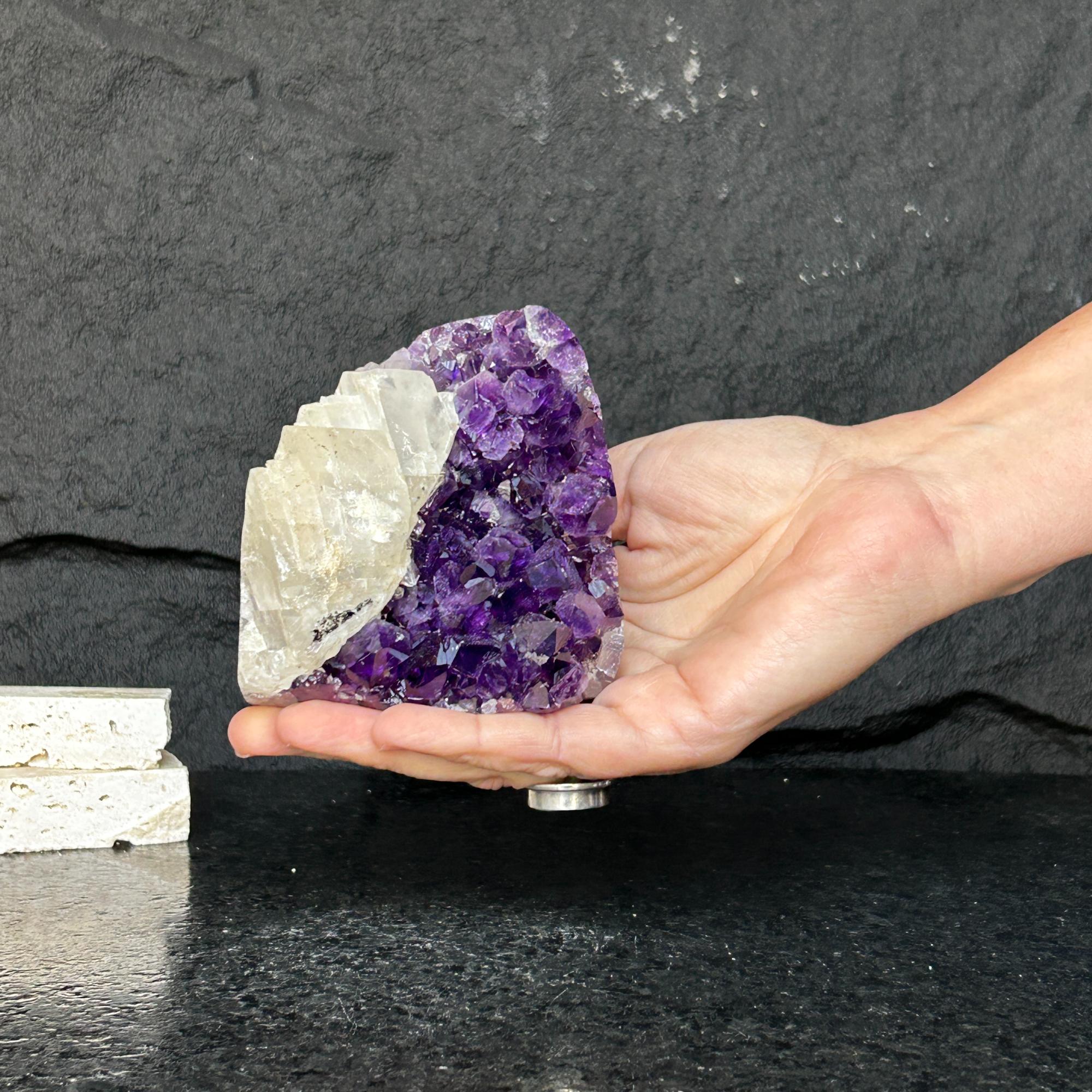 Hand holding a large, raw, deep purple Uruguayan amethyst geode cluster with white rock.