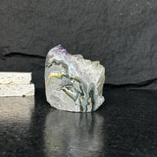 Large, raw amethyst geode with deep purple crystals and colorful mineral veins on a dark surface.