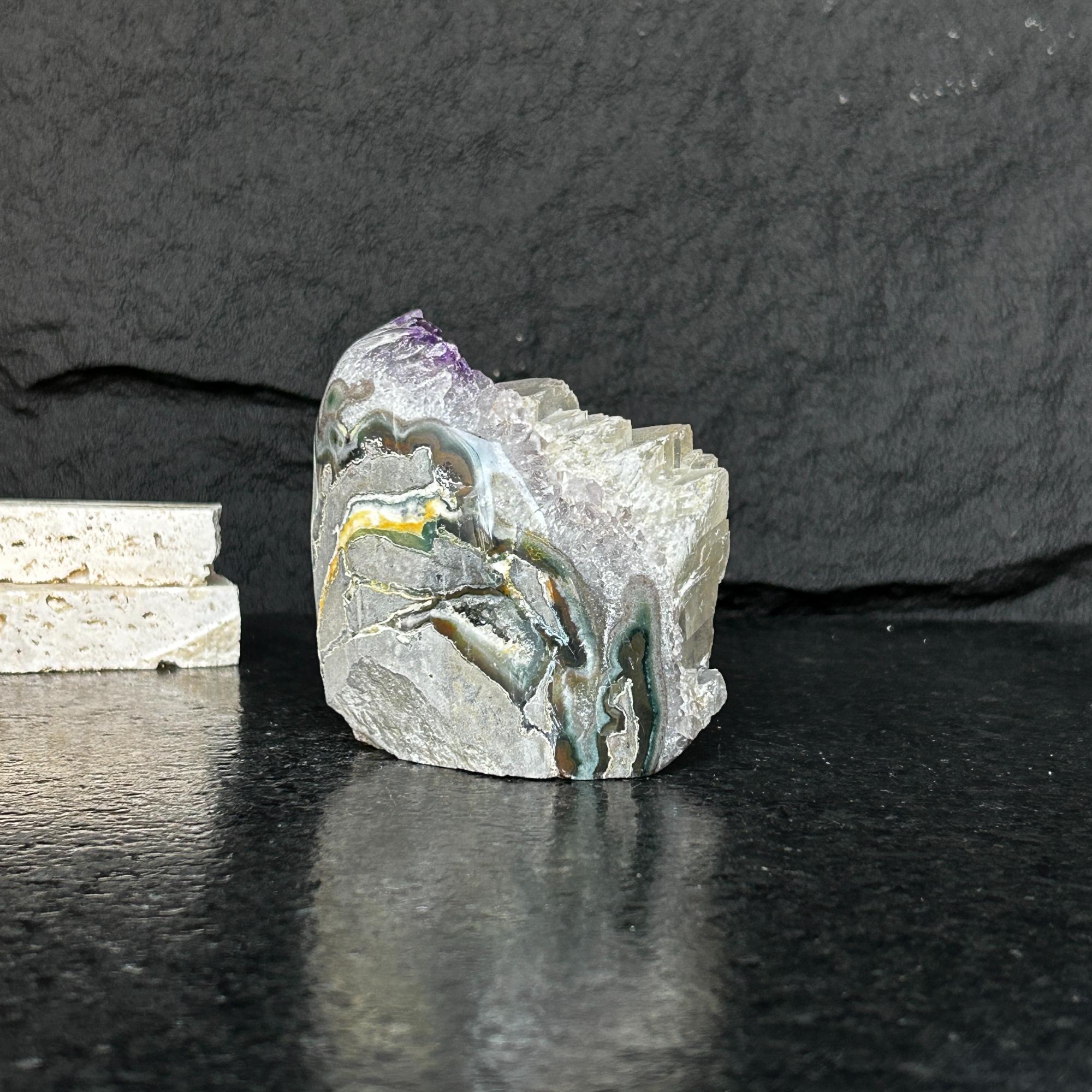 Large, raw amethyst geode with deep purple crystals and colorful mineral veins on a dark surface.