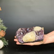 Hand holding a large, deep purple amethyst cluster with prominent crystal points and unique light yellow calcite formations.