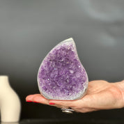 Hand holding a large, polished purple amethyst and agate flame crystal geode.