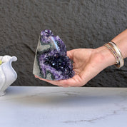 Hand holding a large deep purple amethyst geode cluster with natural calcite and agate formations.