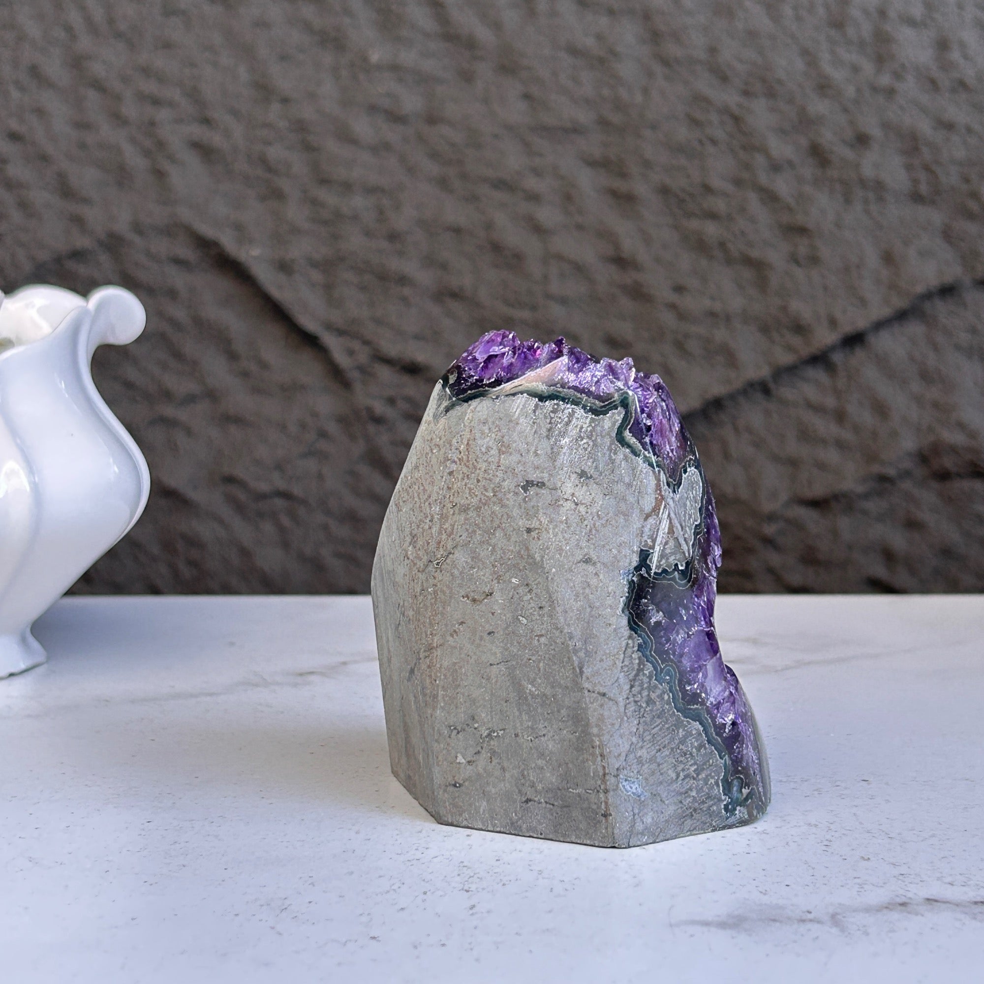 Large amethyst geode with vibrant deep purple crystals and natural gray rock casing.