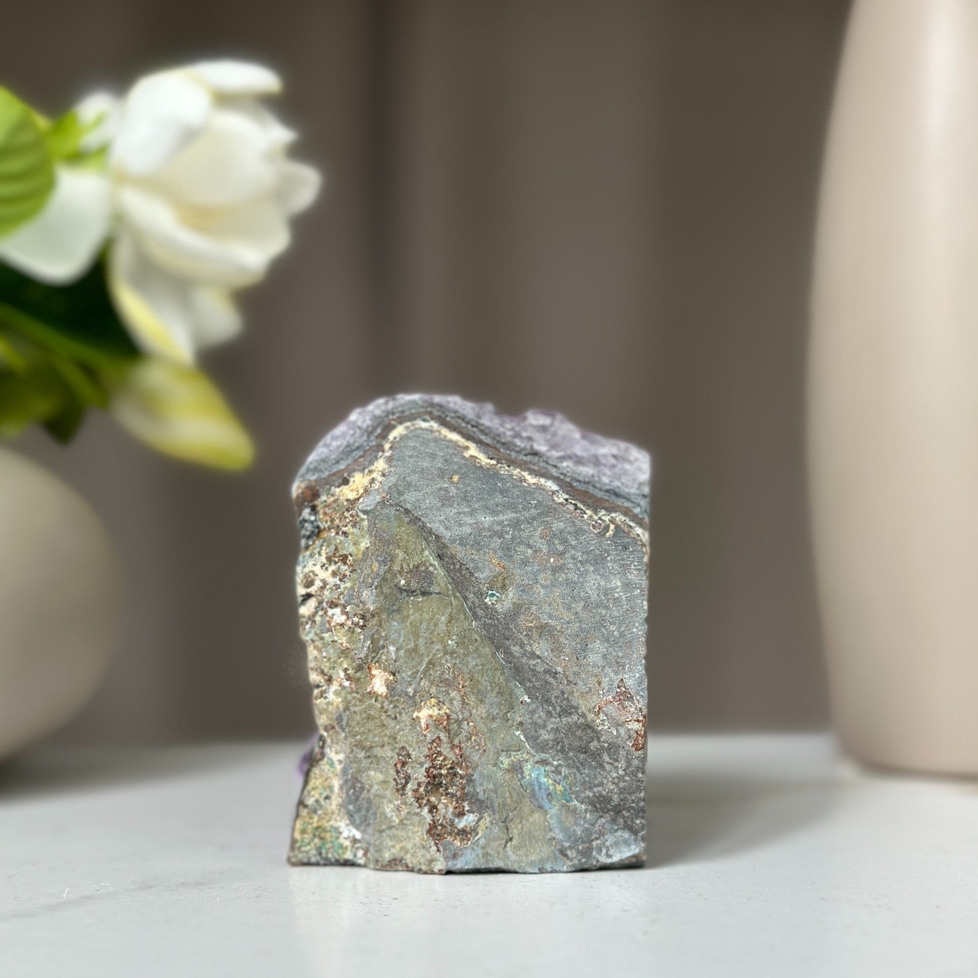 Rough-cut amethyst geode with deep purple crystals and natural grey-green rock face.