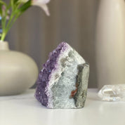 Sparkling lavender amethyst geode cluster with vibrant purple crystals, grey rock, and subtle agate formations.