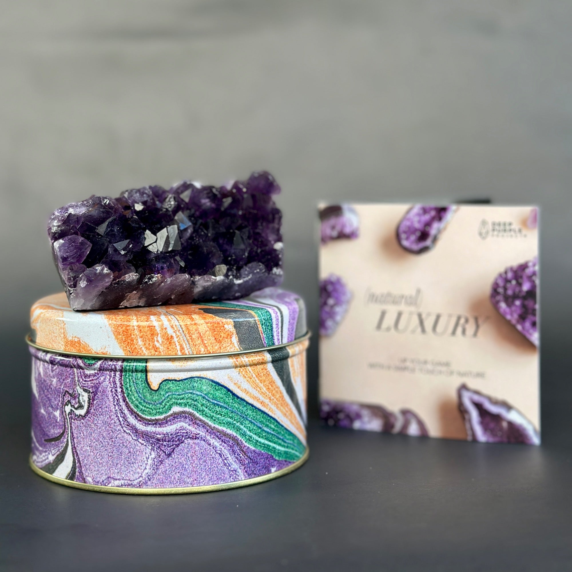 Decorative tin with a purple crystal on top and a box labeled 'Natural Luxury' in the background.
