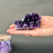 Hand holding a large purple crystal against a neutral background