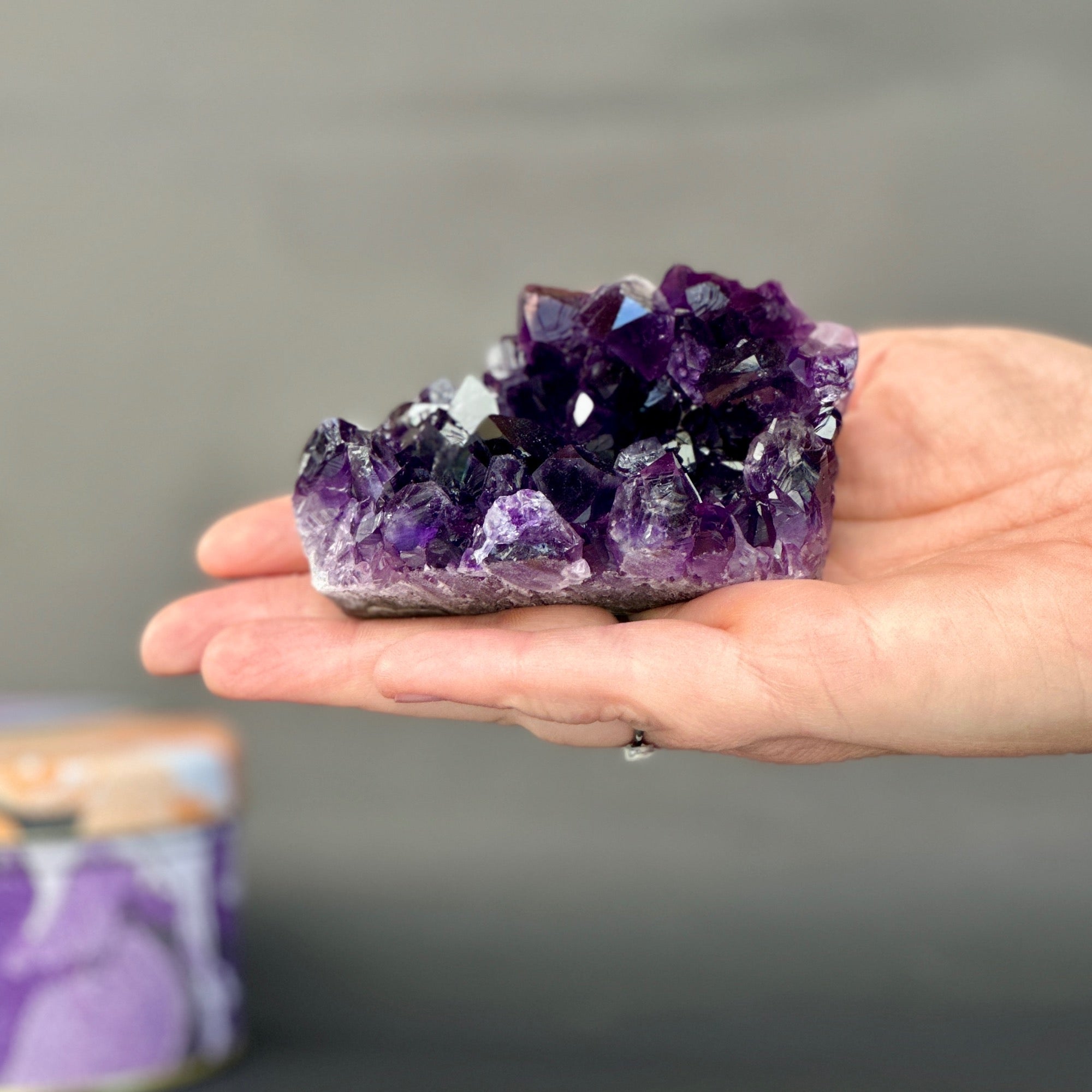 Hand holding a large purple crystal against a neutral background