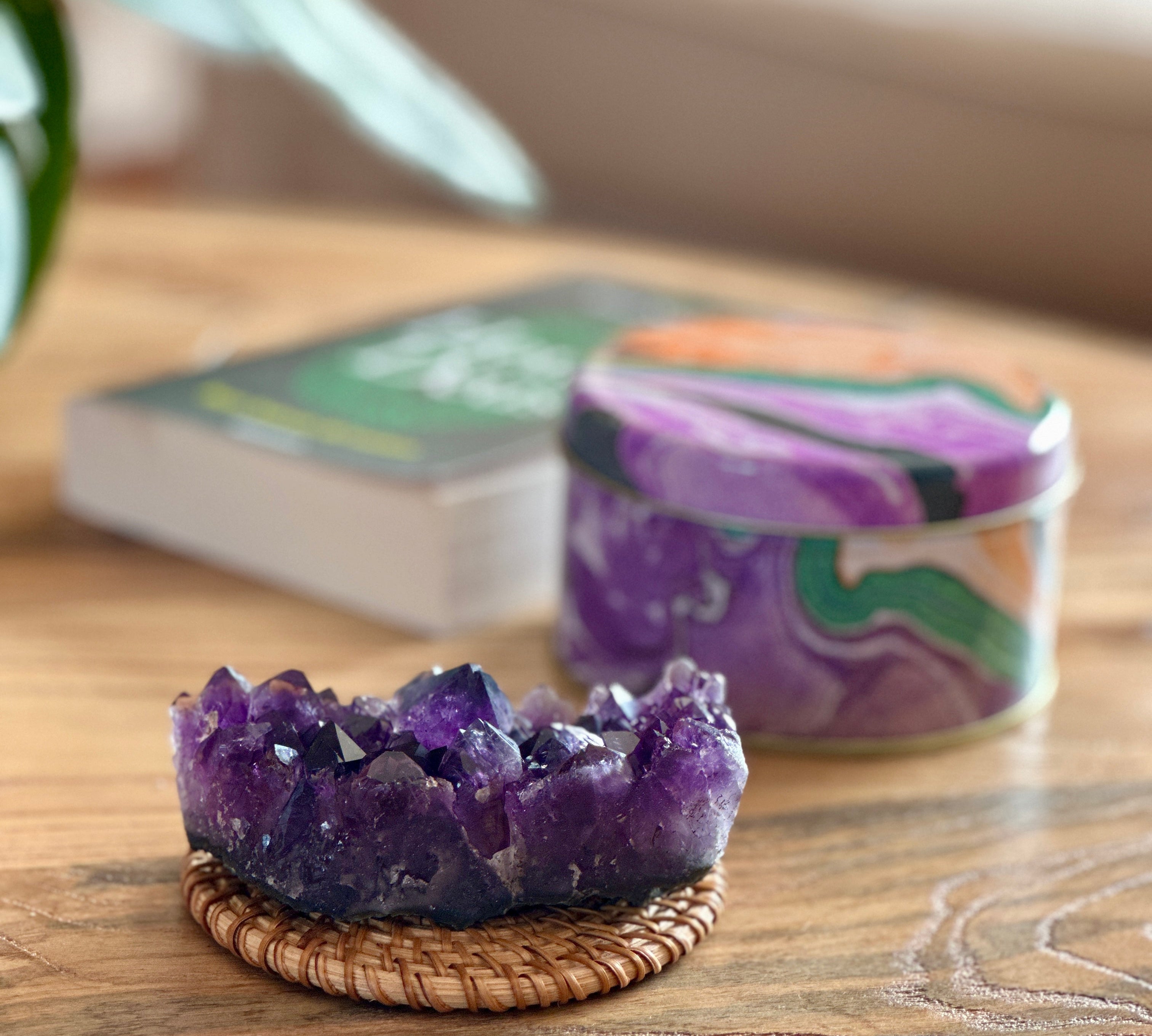 Amethyst crystal on a woven coaster with a candle and book in the background on a wooden surface.