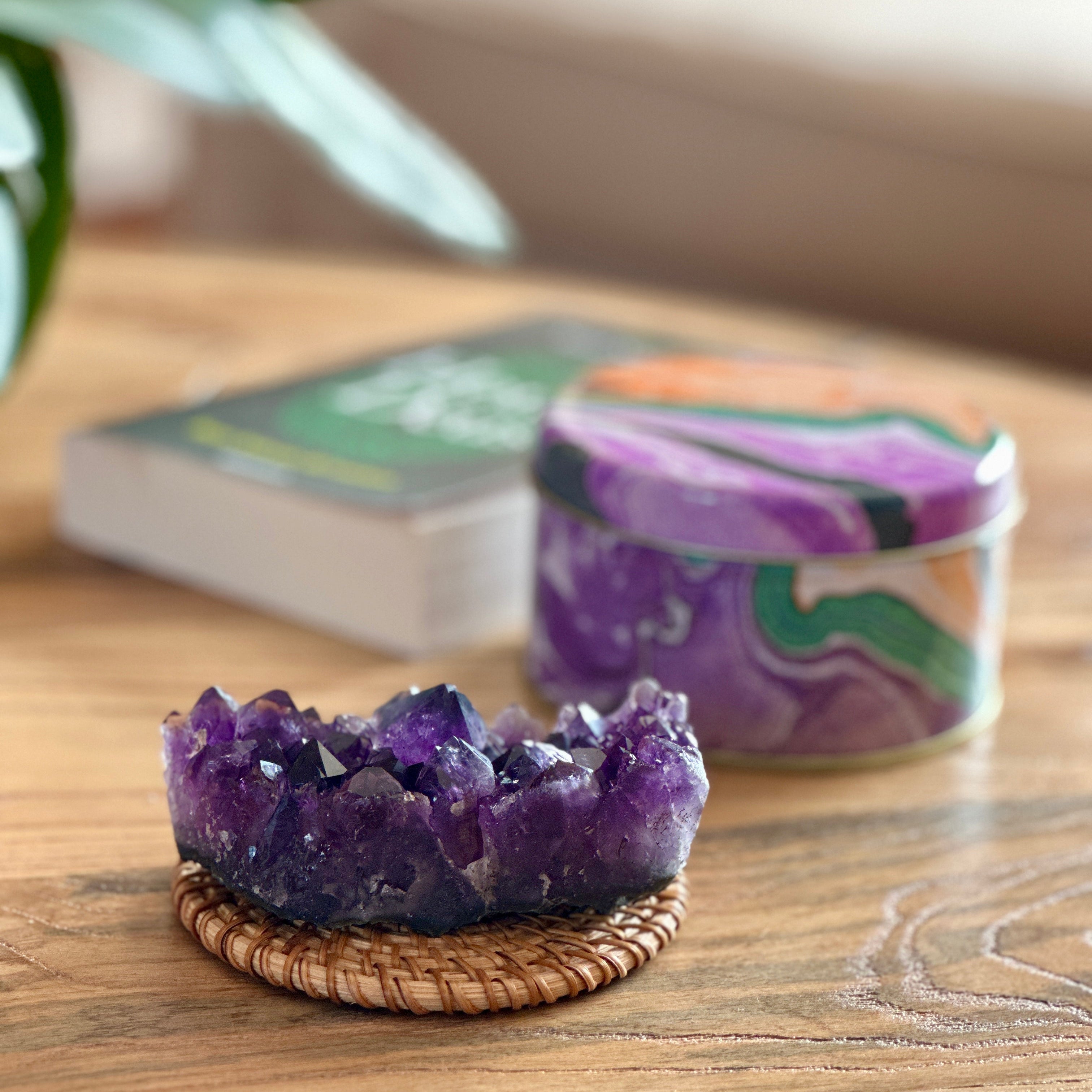 Amethyst crystal on a woven coaster with a candle and book in the background on a wooden surface.