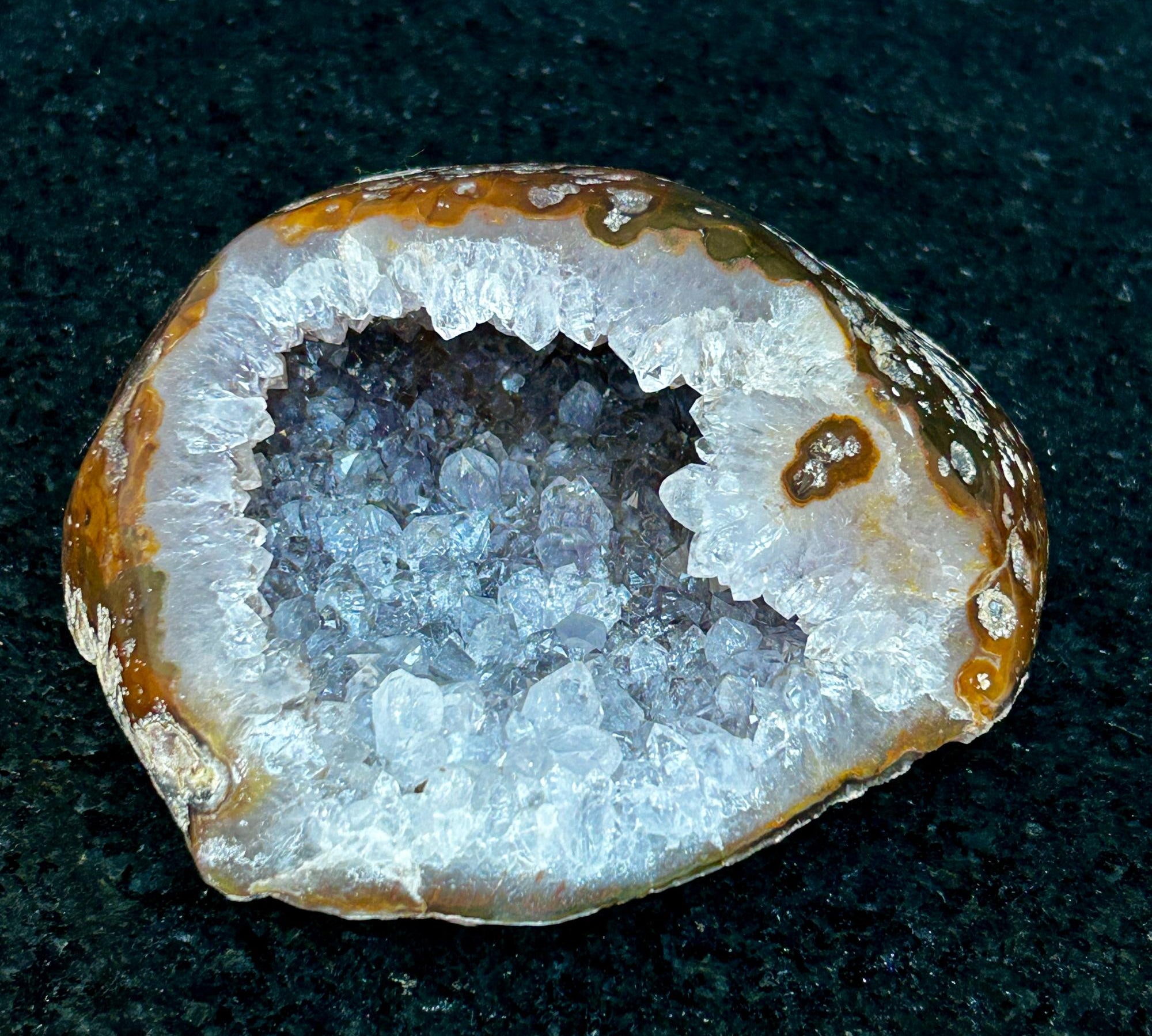 Natural quartz stone geode with sparkling white and purple crystals, brown agate rim, flat Uruguayan cave.