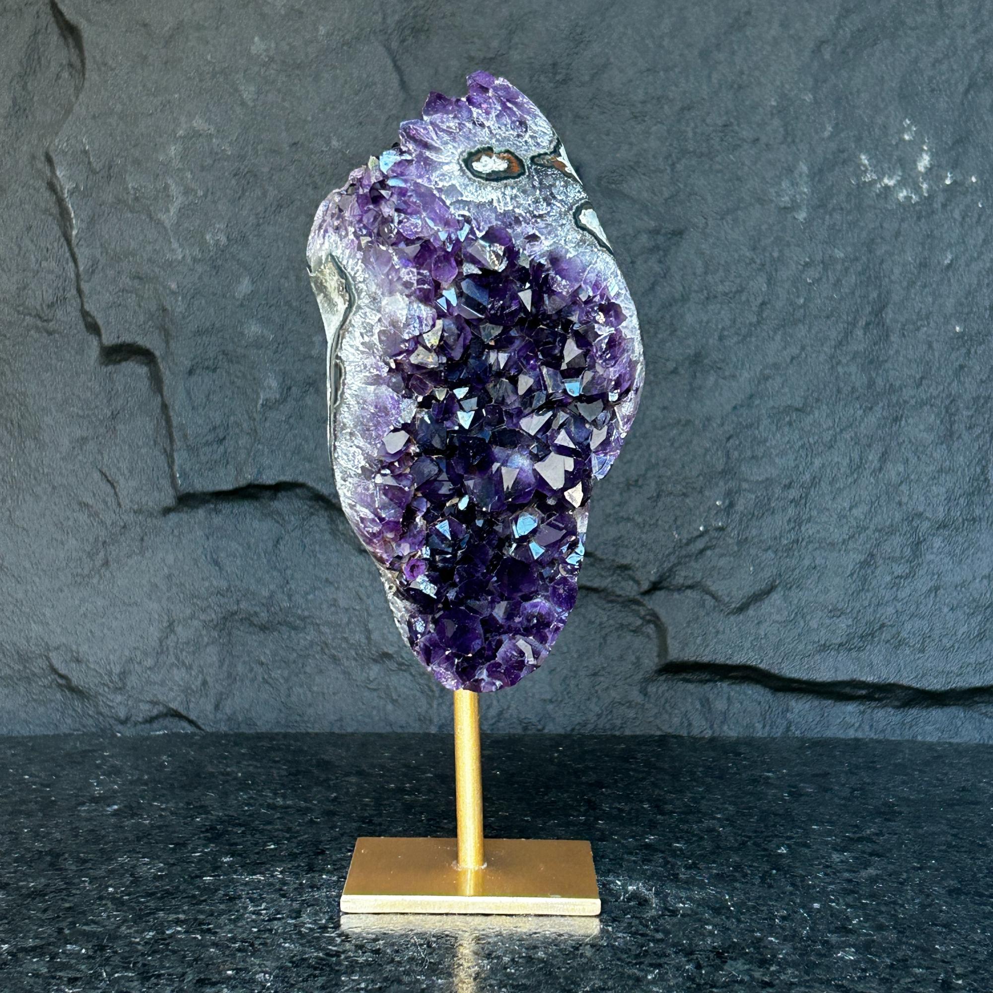 Natural Uruguayan amethyst cave, deep purple crystals on a gold metal stand, against a dark background.