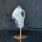Natural Uruguayan amethyst cave on a gold metal stand, featuring deep purple crystals and a polished gray exterior.
