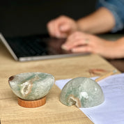 Two green stones on a wooden surface with a person using a laptop in the background.