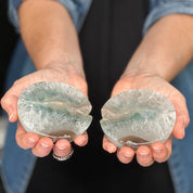 Two hands holding half-cut agate stones against a blurred background.