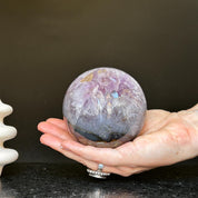 Polished deep violet amethyst sphere with white and black agate formations, held in a hand.