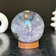 Polished deep violet amethyst sphere with white and black agate formations on a carob wood base.