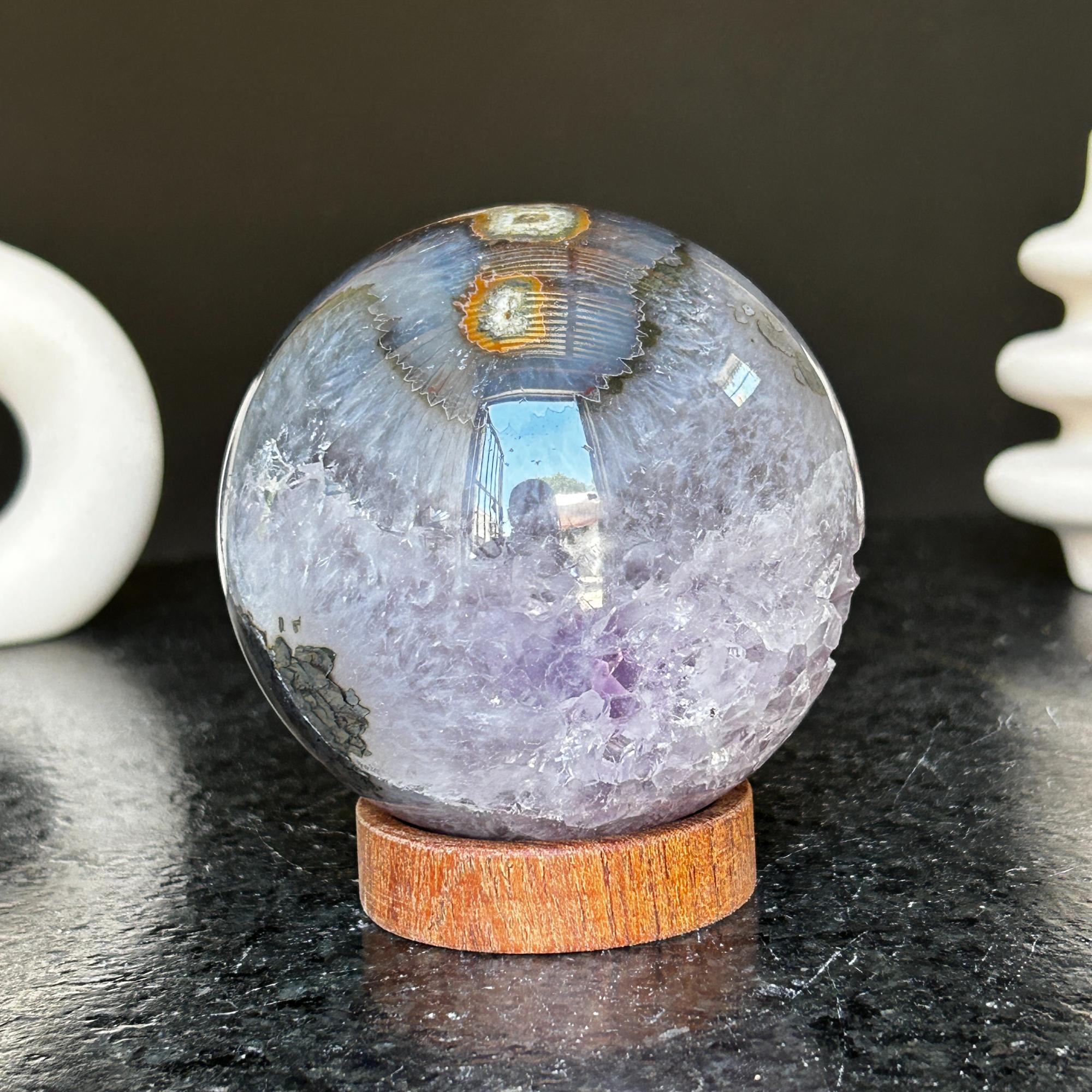 Polished deep violet amethyst sphere with white and black agate formations on a carob wood base.