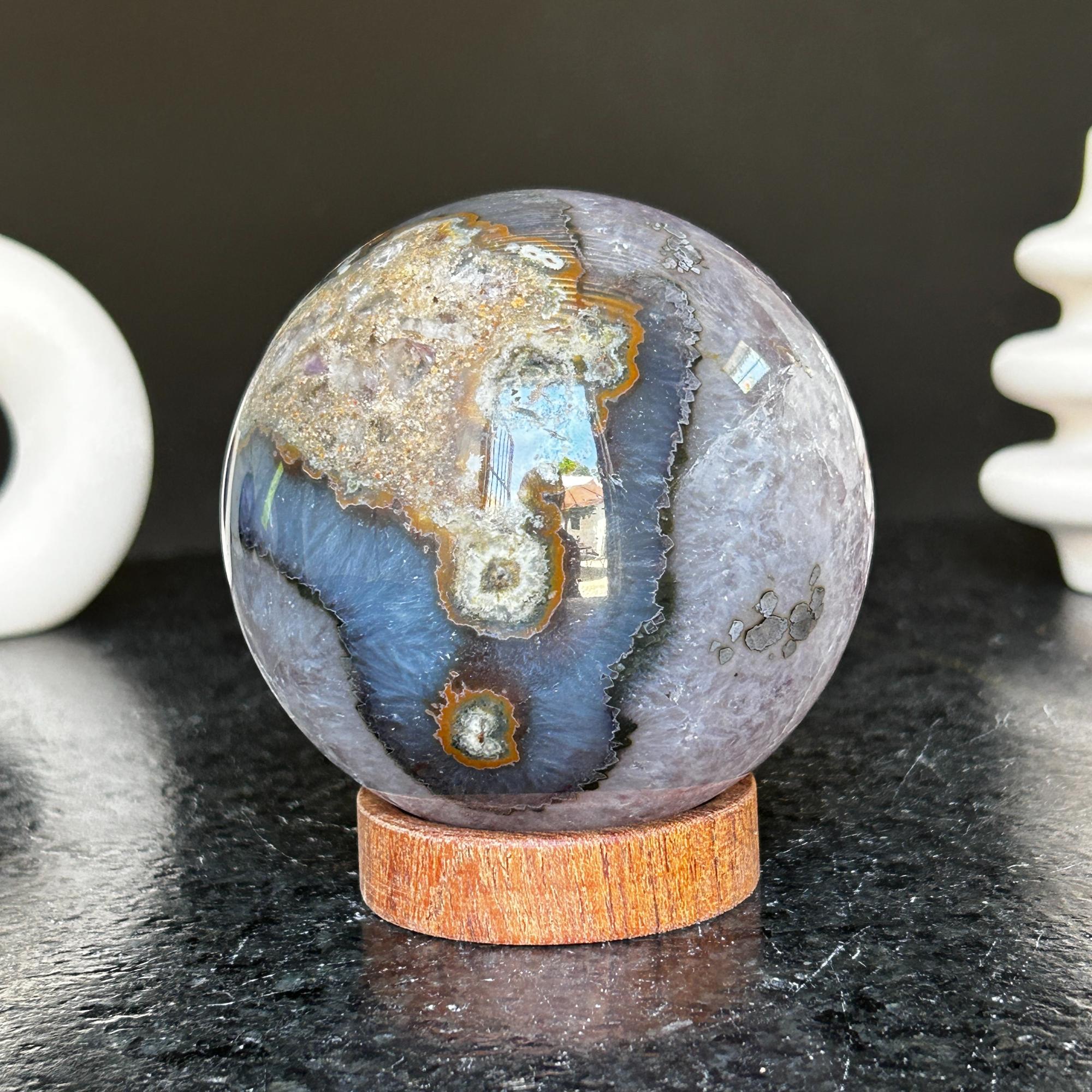Polished deep violet amethyst sphere with white and black agate formations on a carob wood base.