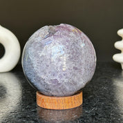 Polished deep violet amethyst sphere with white and black agate details on a carob wood base.