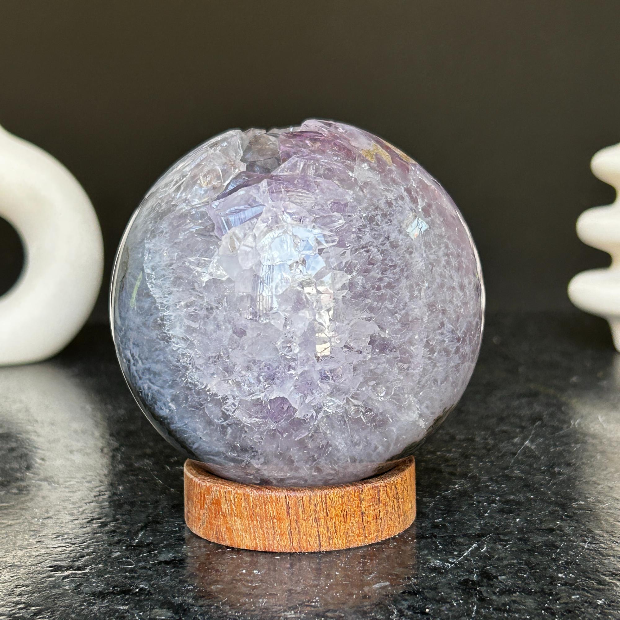Polished deep violet amethyst sphere with white and black agate details on a carob wood base.