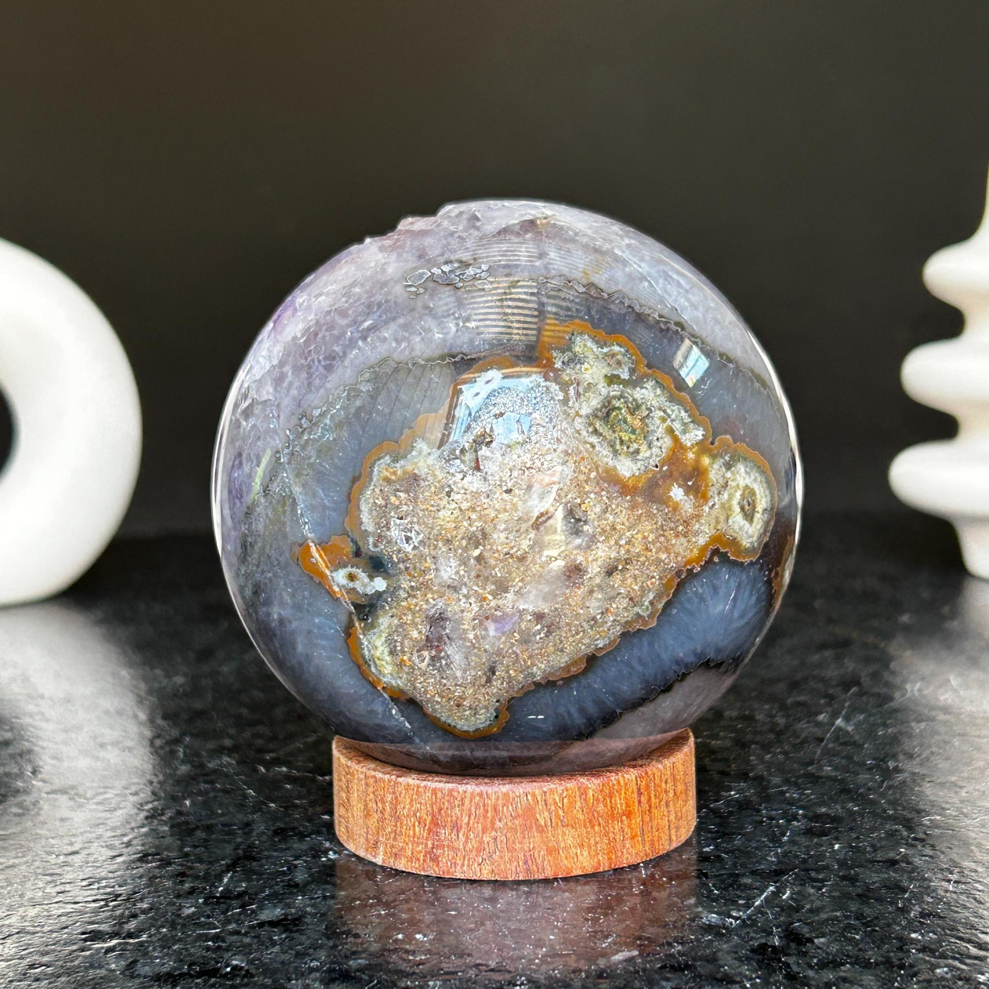 Polished deep violet amethyst sphere with white and black agate formations on a carob wood base.