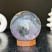 Polished deep violet amethyst sphere with white and black agate formations on a carob wood base.