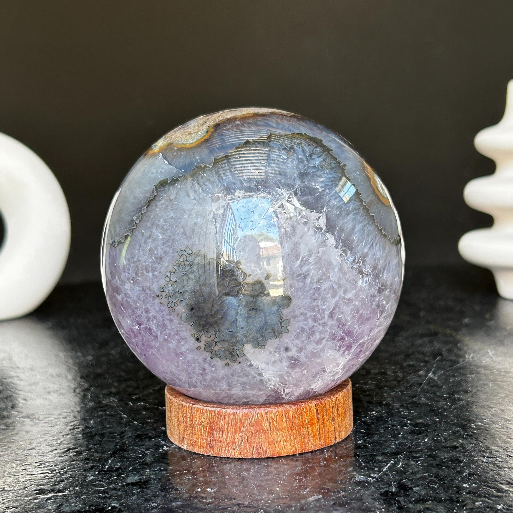 Polished deep violet amethyst sphere with white and black agate formations on a carob wood base.