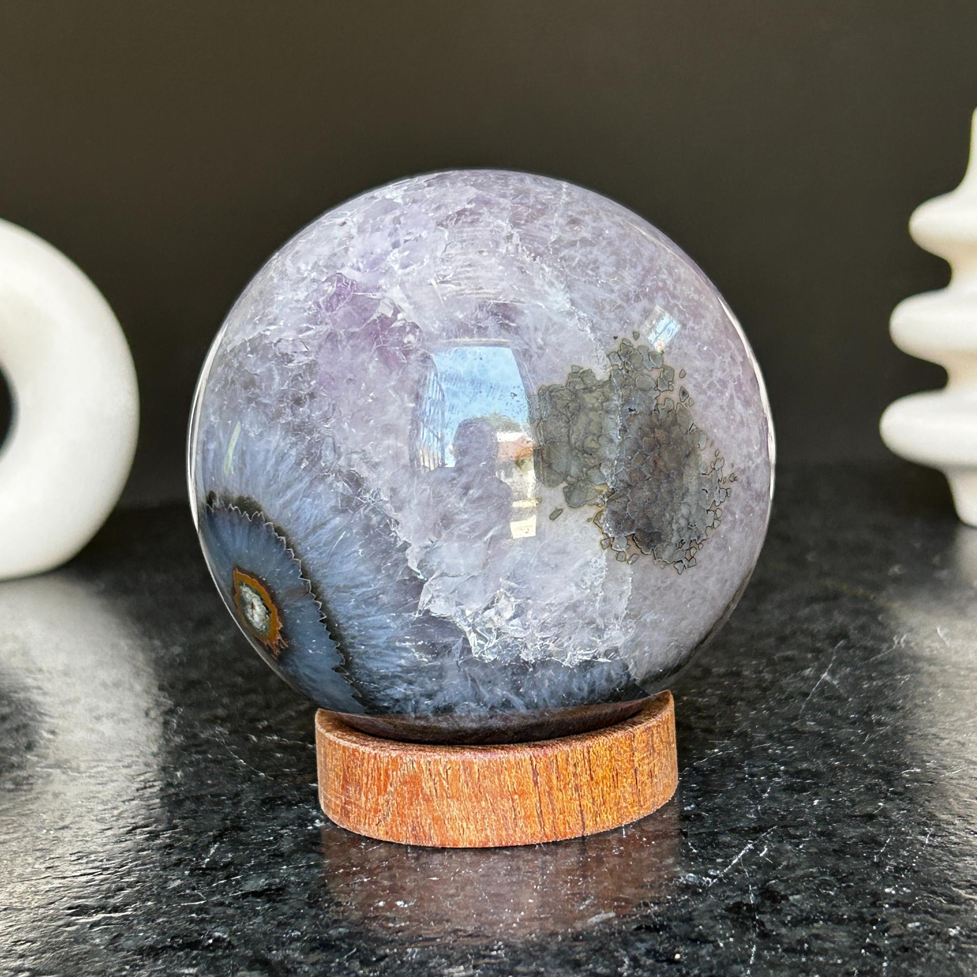 Polished deep violet amethyst sphere with white and black agate formations on a carob wood base.