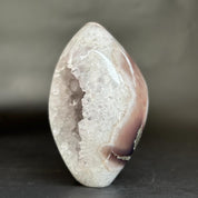 A polished natural agate crystal geode with a smooth teardrop shape, showcasing a white crystalline interior and a smooth outer band of dusty pink and light brown.