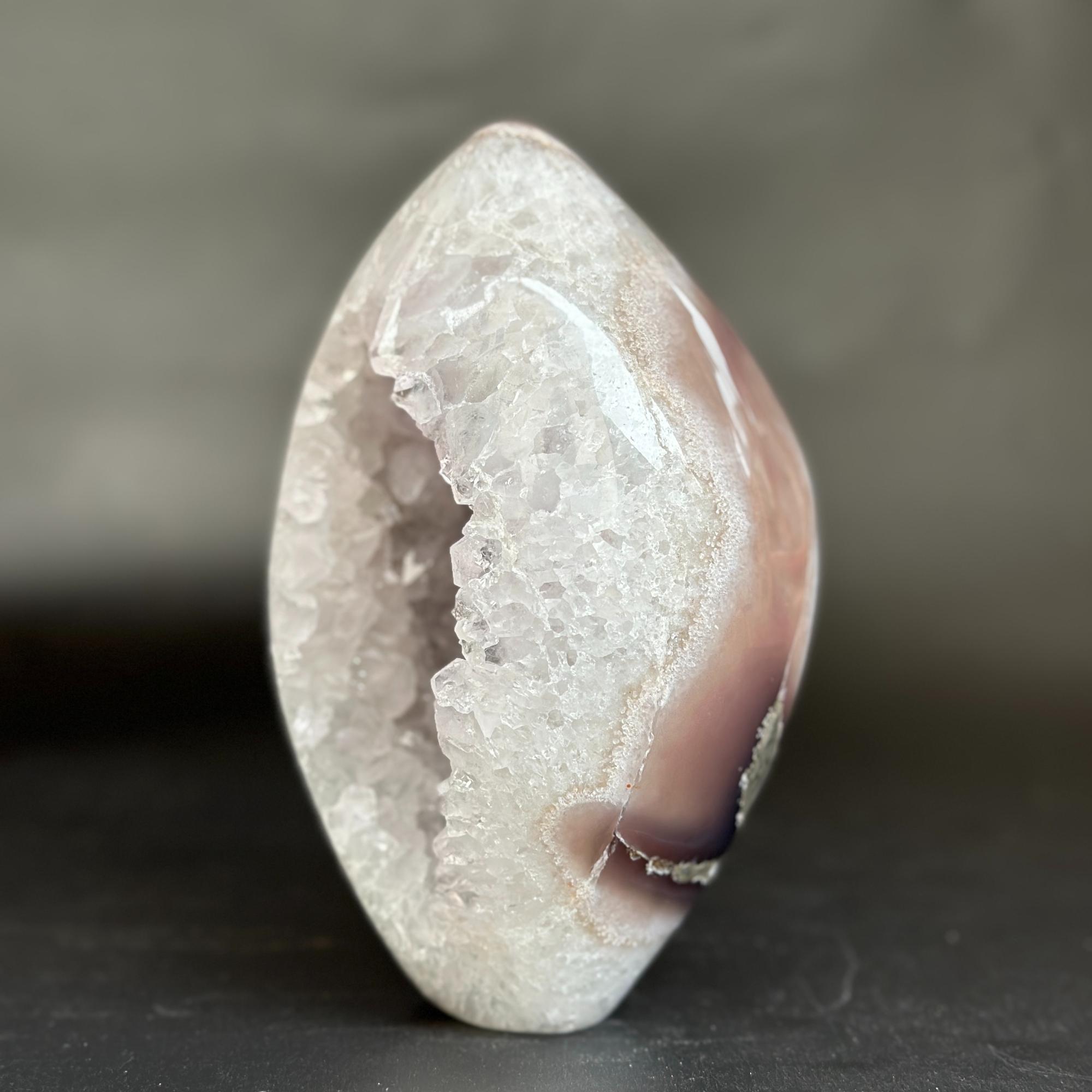 A polished natural agate crystal geode with a smooth teardrop shape, showcasing a white crystalline interior and a smooth outer band of dusty pink and light brown.