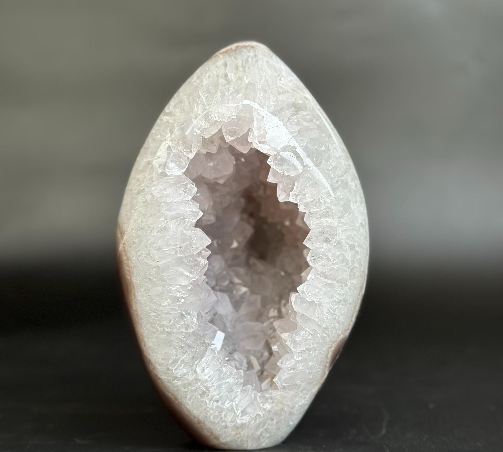 A polished geode specimen with a smooth, rounded outer shell and a crystalline interior, photographed against a dark gray background.