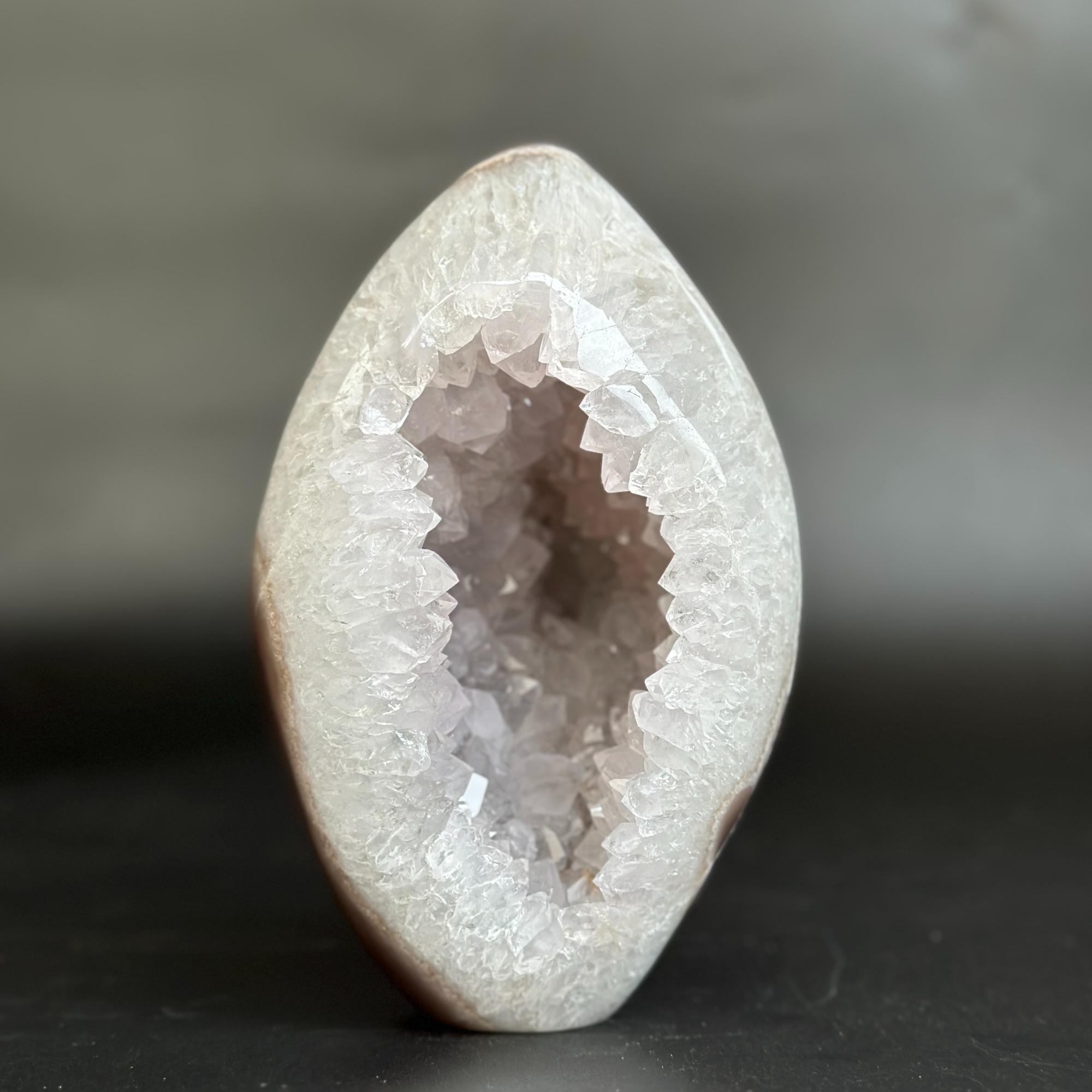 A polished geode specimen with a smooth, rounded outer shell and a crystalline interior, photographed against a dark gray background.