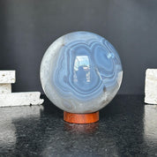 Large polished quartz and agate sphere with gray and black layers on a carob wood base.
