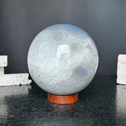 Large 4-inch quartz and agate sphere with gray and black layers, on a carob wood base.