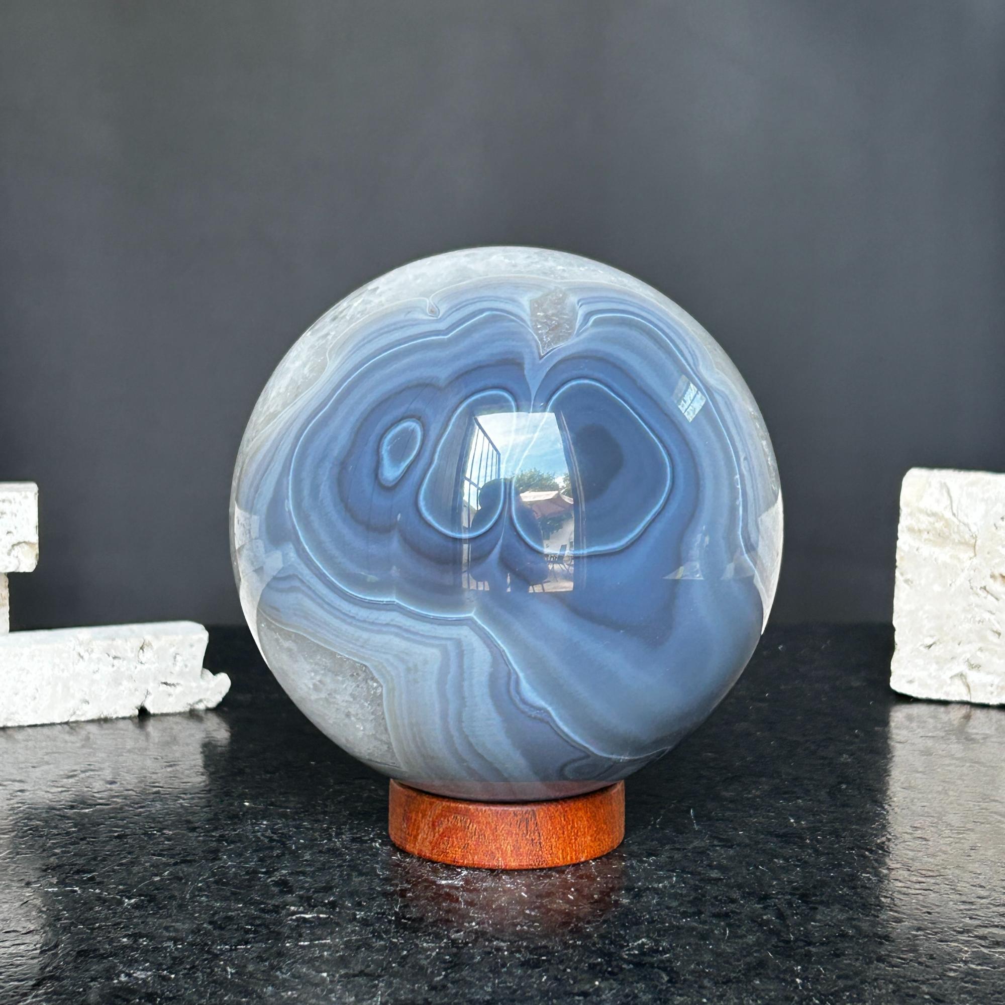 Large polished quartz and agate sphere with blue, gray, and white layers on a carob wood base.