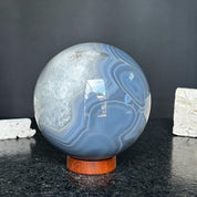 Large polished quartz and agate sphere with gray and black layers on a carob wood base.