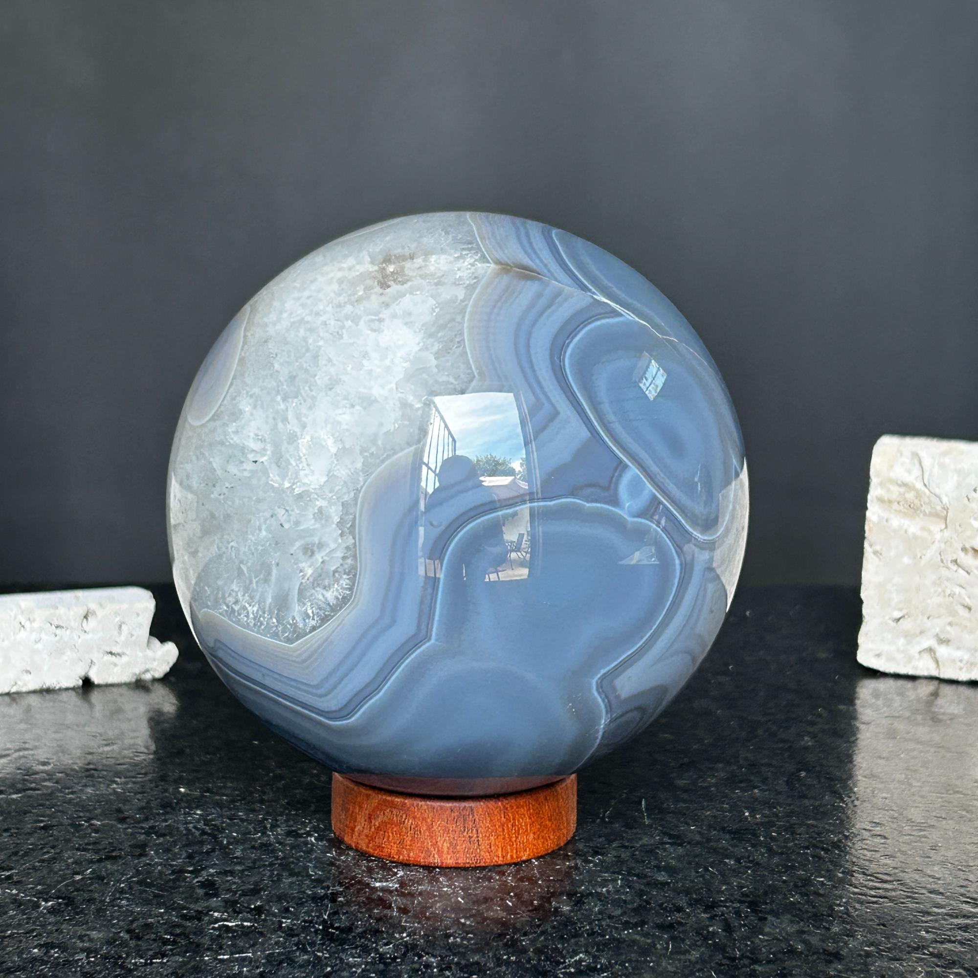 Large polished quartz and agate sphere with gray and black layers on a carob wood base.