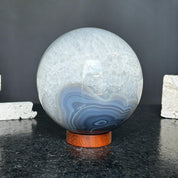 Polished quartz and agate sphere with gray and black layers on a round carob wood base.