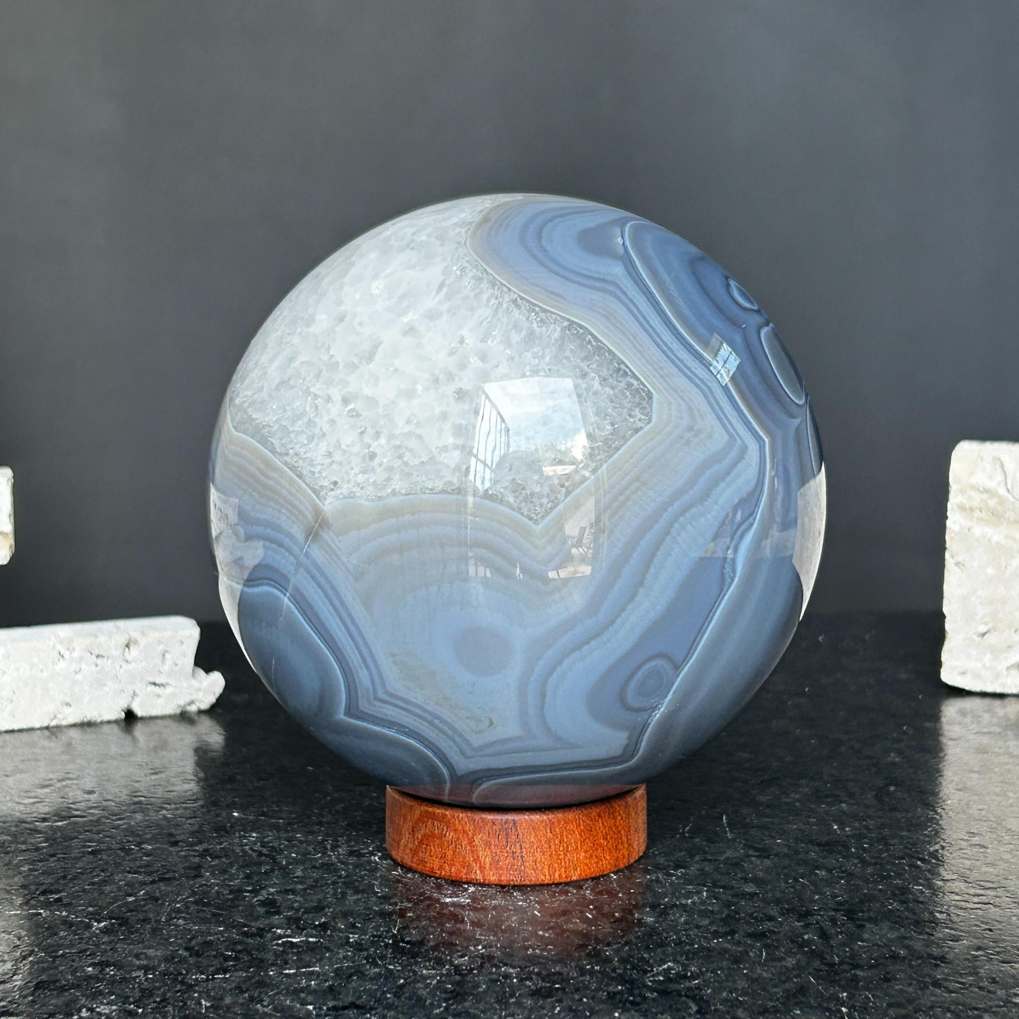 Large polished quartz and agate sphere with gray and black layers, on a carob wood base.