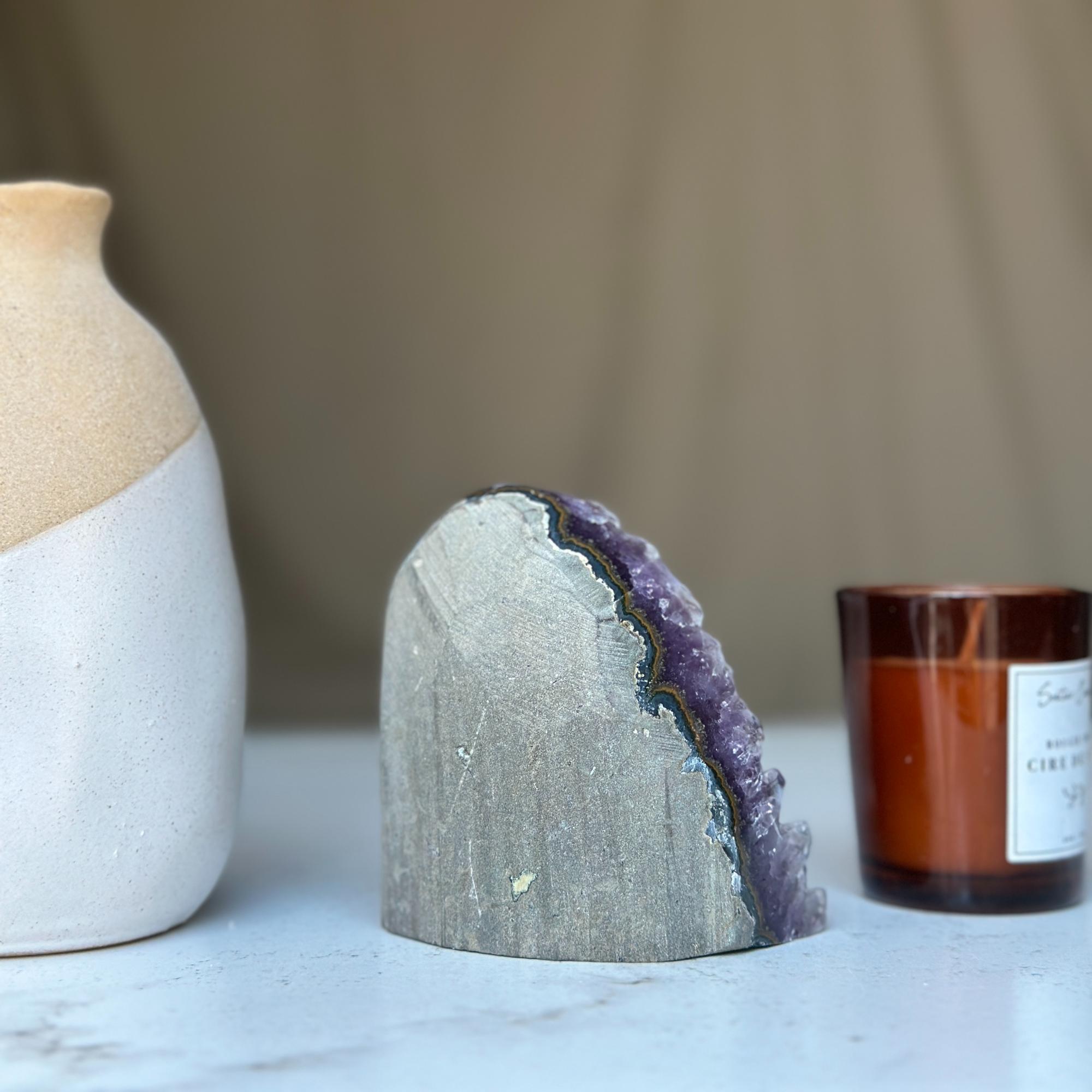 Raw amethyst geode cluster featuring vibrant deep purple crystals and a rough grey exterior.