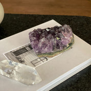 Deep purple raw flat amethyst cluster from Uruguay on a white book, with a clear quartz crystal.