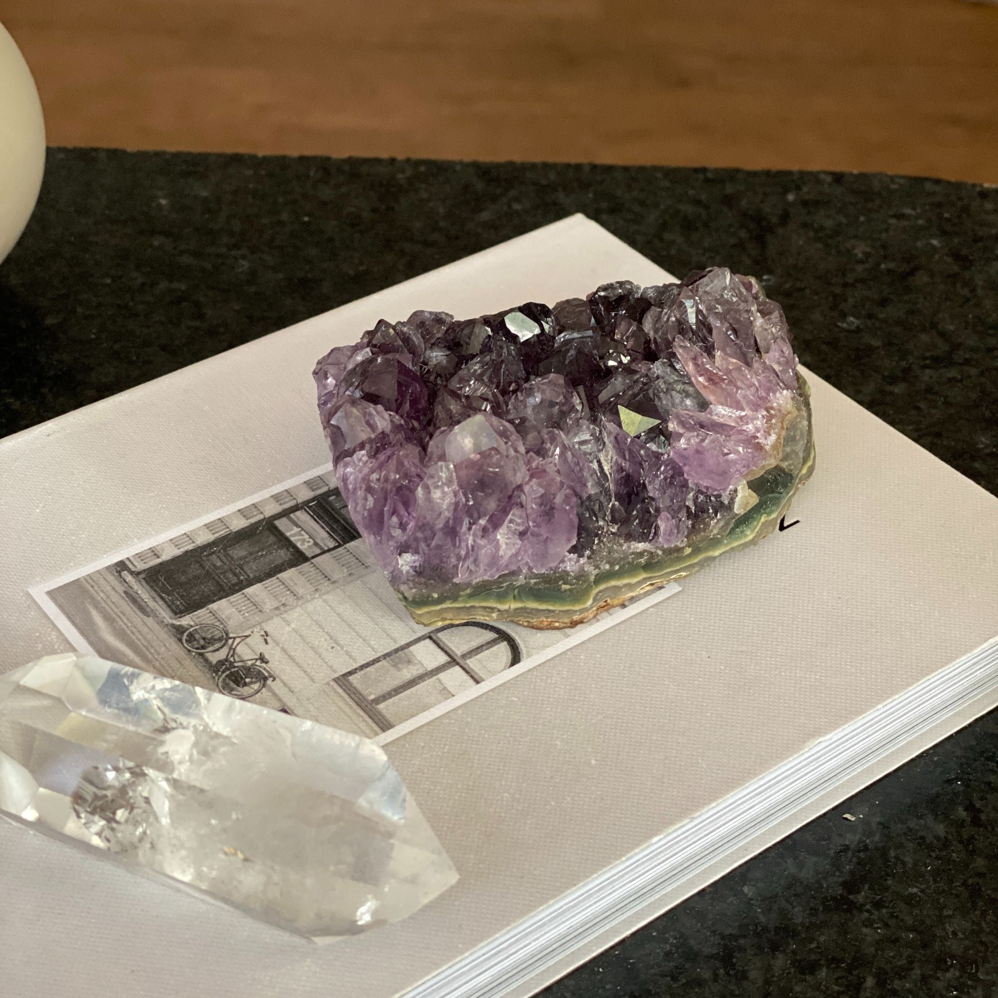 Deep purple raw flat amethyst cluster from Uruguay on a white book, with a clear quartz crystal.