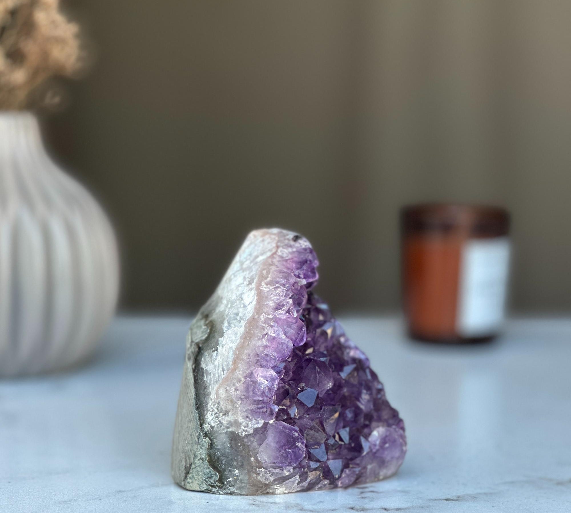 Raw purple amethyst geode crystal cluster, 3.5 in tall, on a white marble surface.