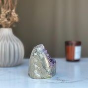 Raw purple amethyst geode cluster, 3.5-inch tall, with a grey exterior, on a white surface.