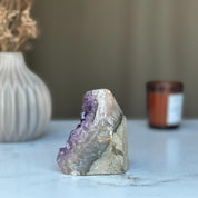Raw purple amethyst geode crystal cluster, 3.5 in tall, on a white marble surface.