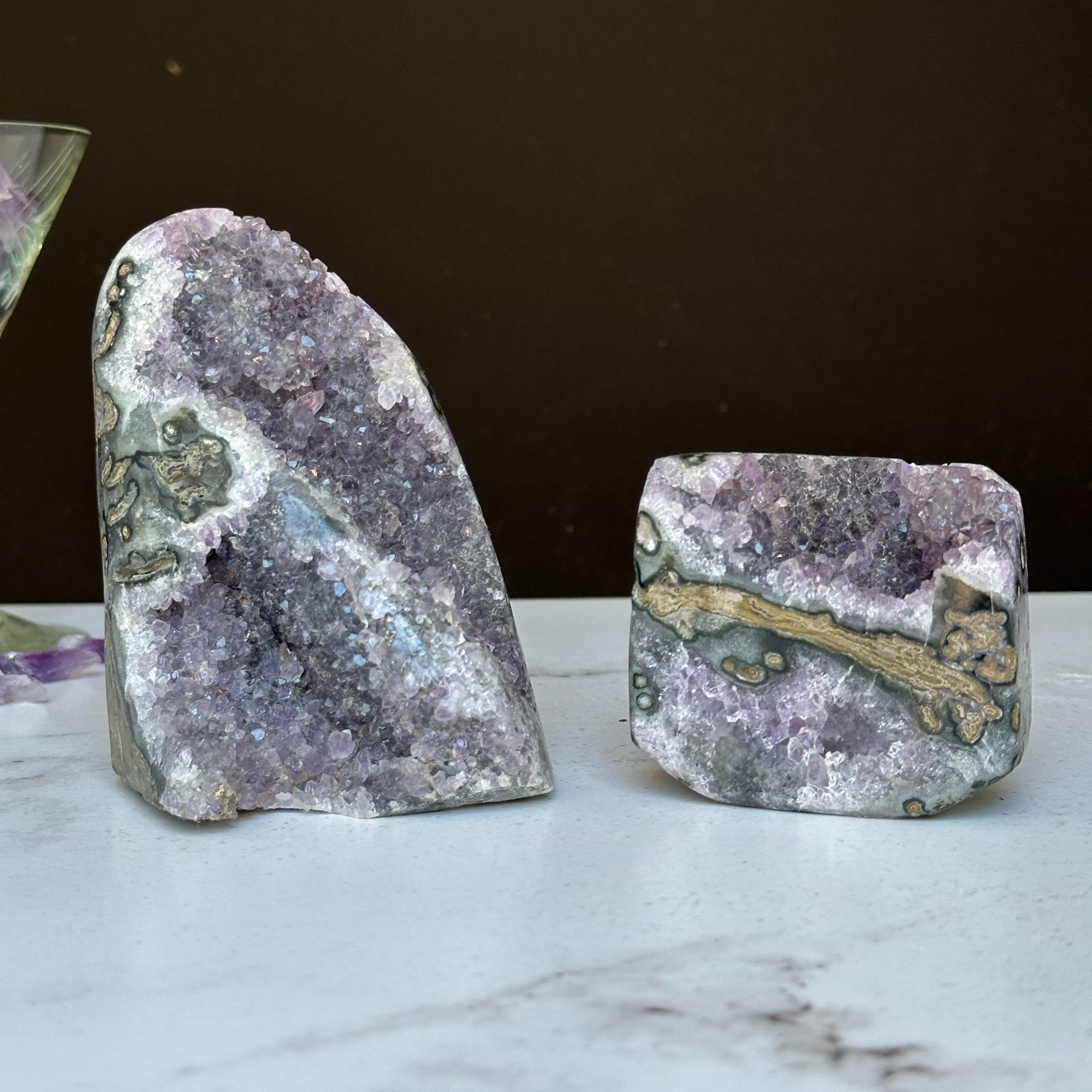 Two vibrant Uruguayan amethyst geode clusters with agate formations, one tall and one shorter.