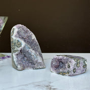Two vibrant purple amethyst geode clusters with agate formations, one large and one small, on a white surface.