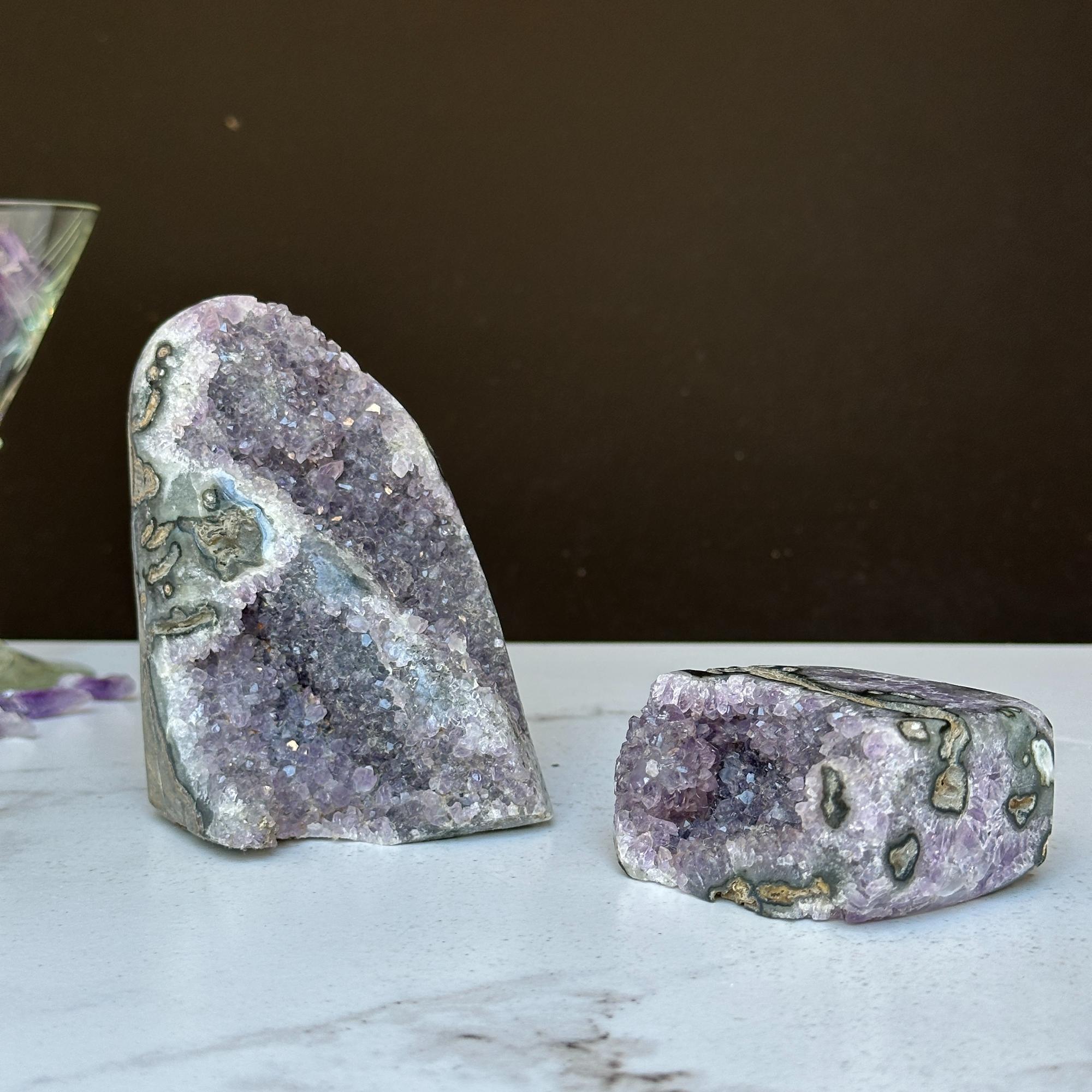 Two vibrant purple amethyst geode clusters with agate formations, one large and one small, on a white surface.